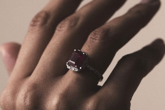 Ruby and diamond halo ring shown in a hand
